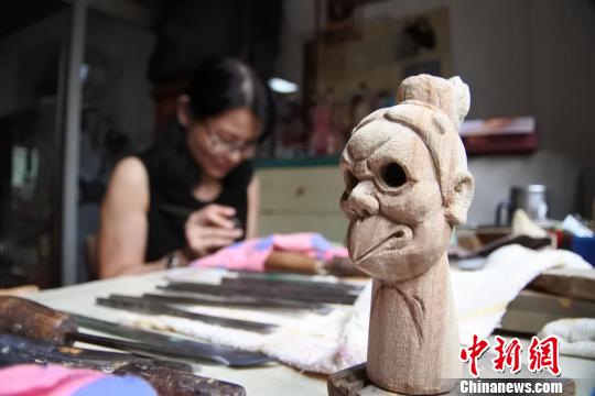 新雕刻出来的木偶头造型与正在埋头工作的“江加走木偶头”传承人相映成趣。 廖静 摄 新雕刻出来的木偶头造型与正在埋头工作的“江加走木偶头”传承人相映成趣。 廖静 摄